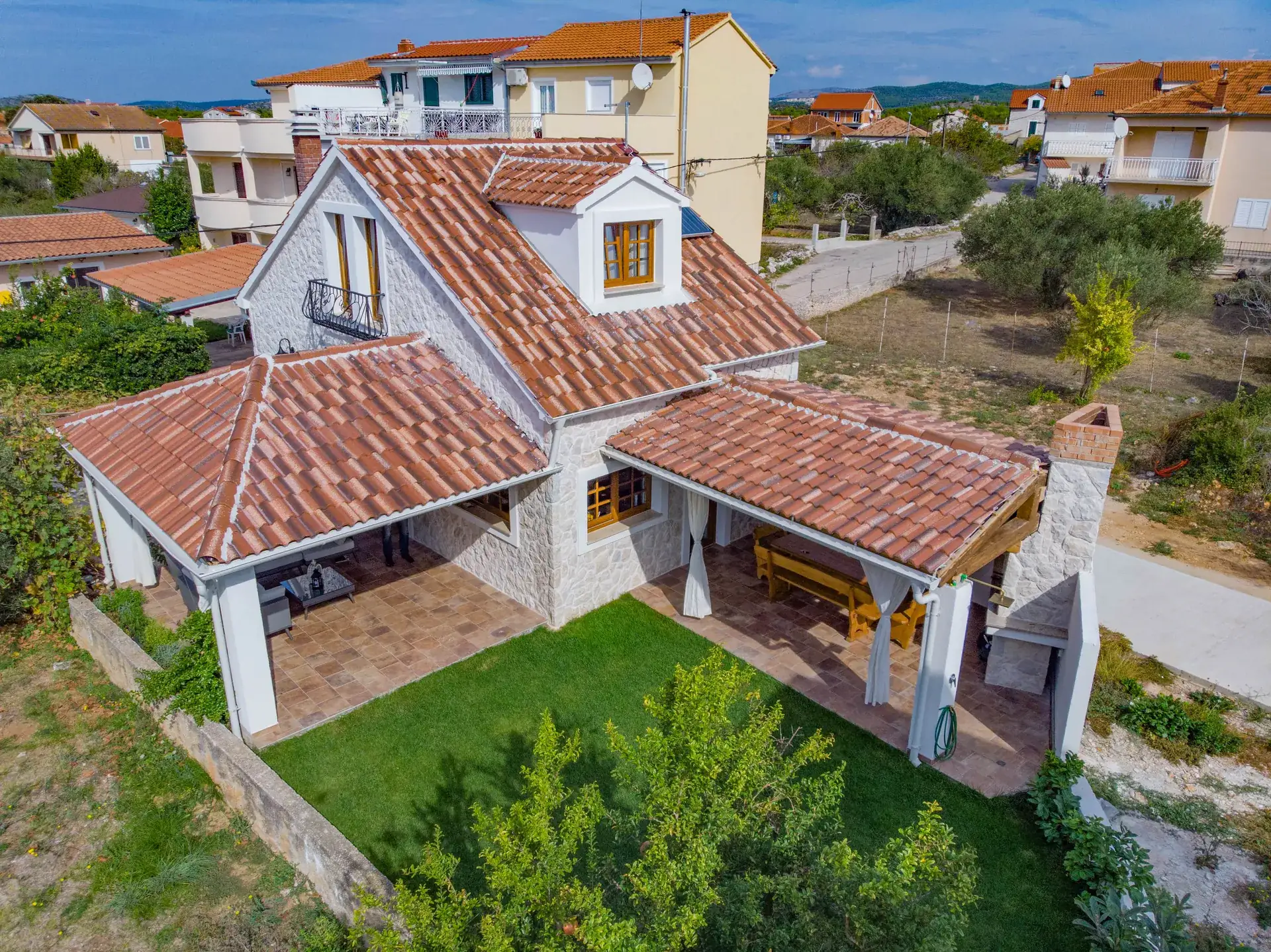Aerial view of House Leila, a stone holiday home with a tiled roof, covered terrace and green garden in Zablaće near Šibenik