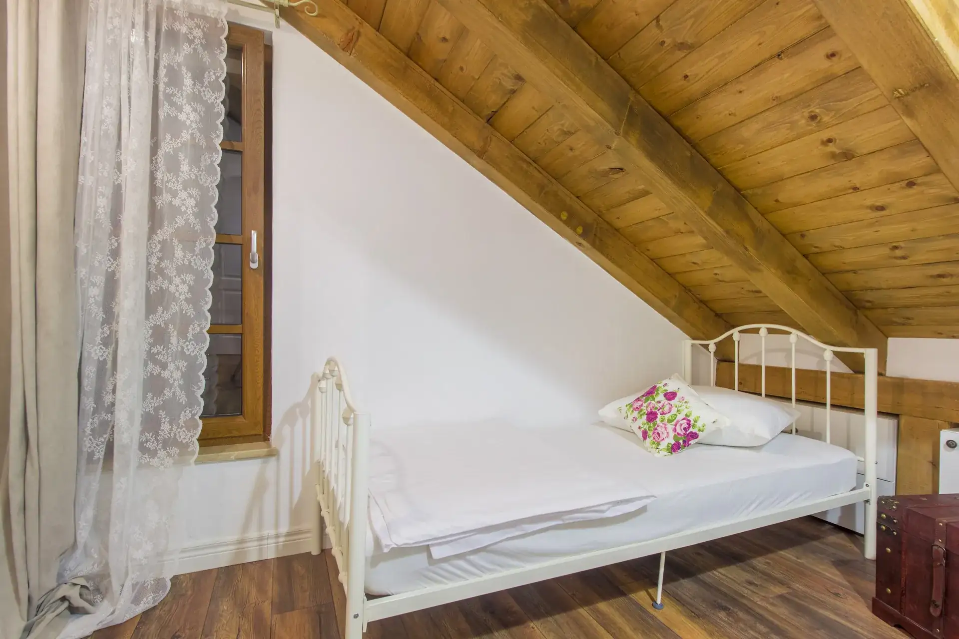Bedroom under the pitched wooden roof with a white iron bed