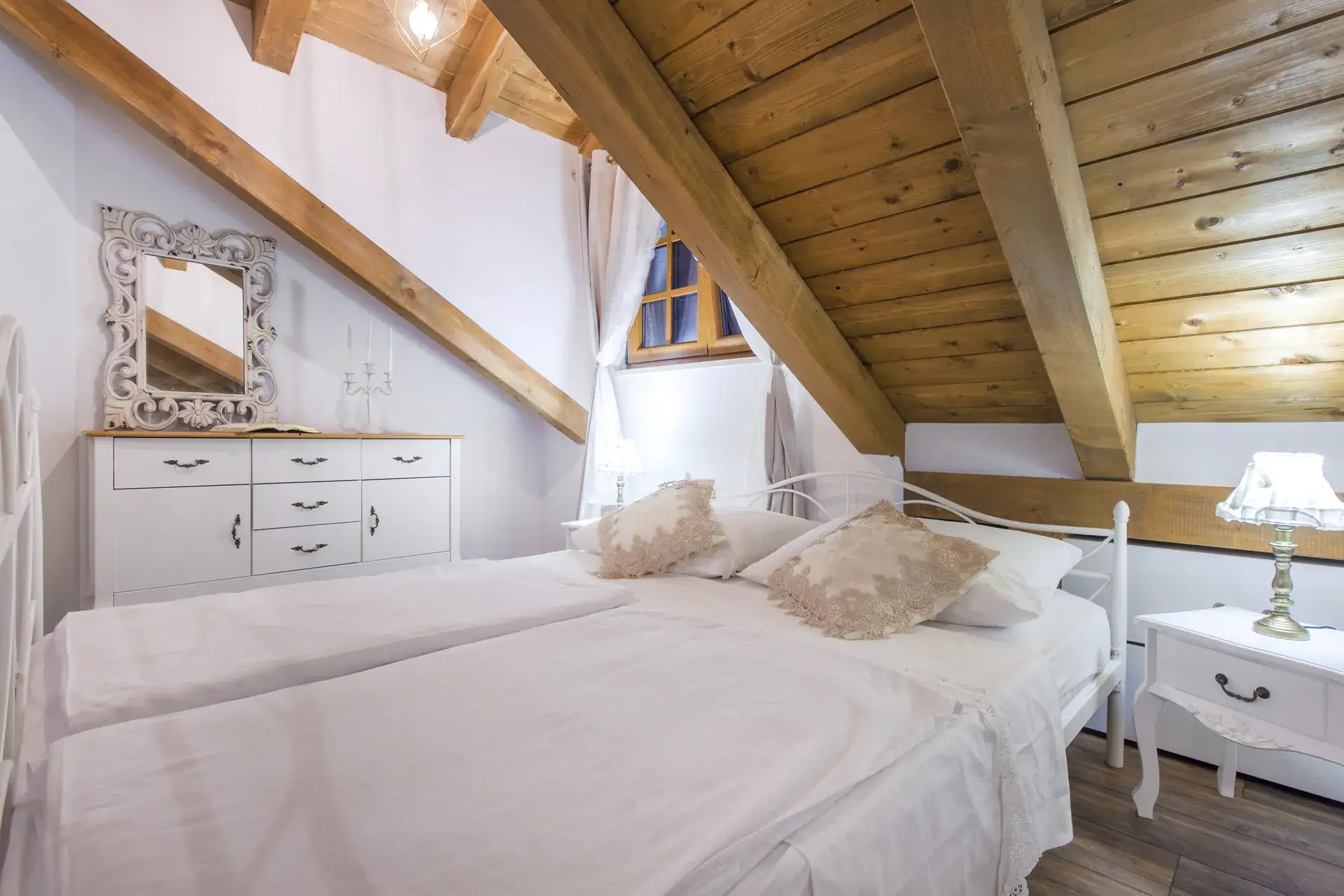 Bedroom with a double bed, white dresser and mirror under the wooden ceiling