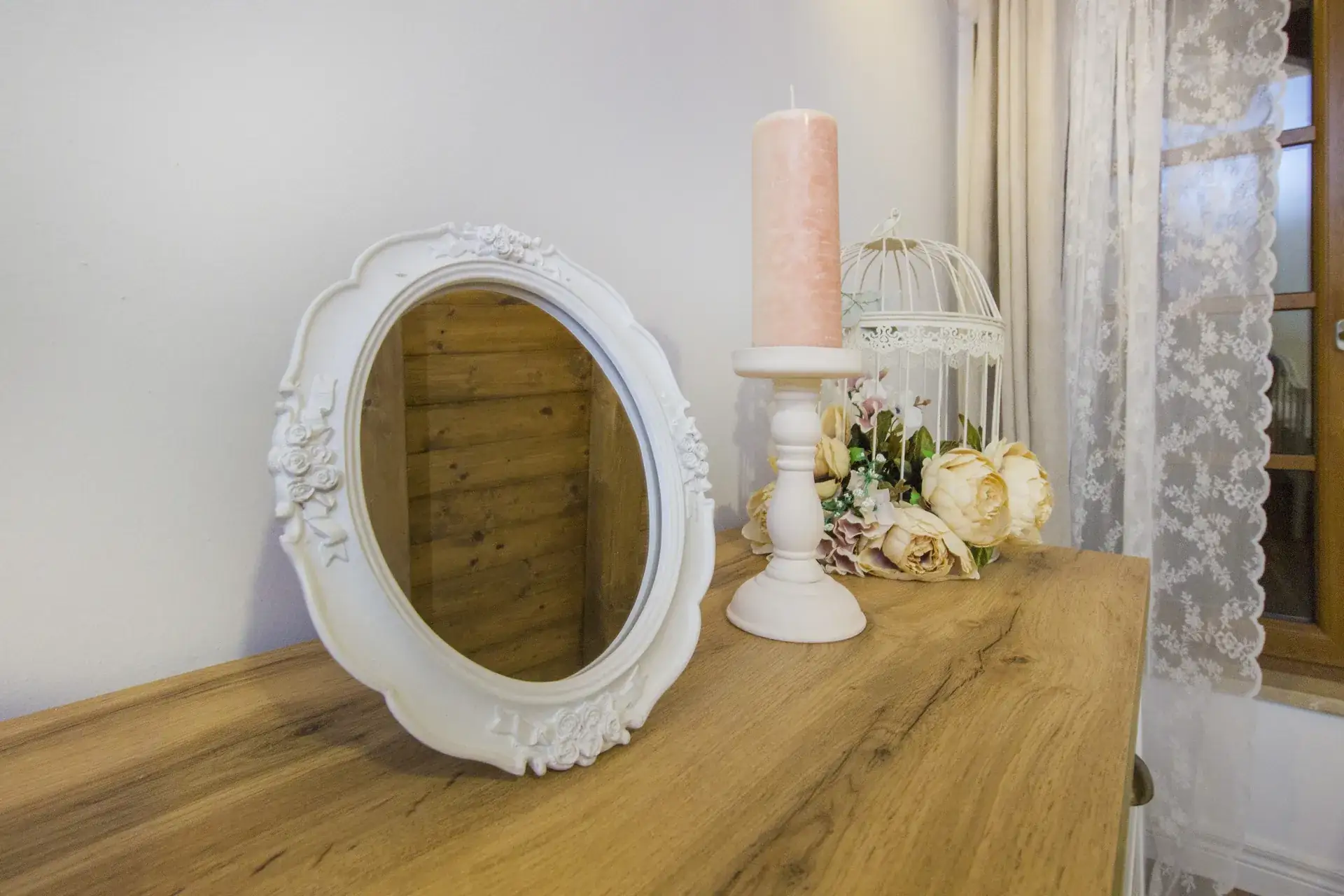 Oval mirror, candle and flowers on the wooden dresser