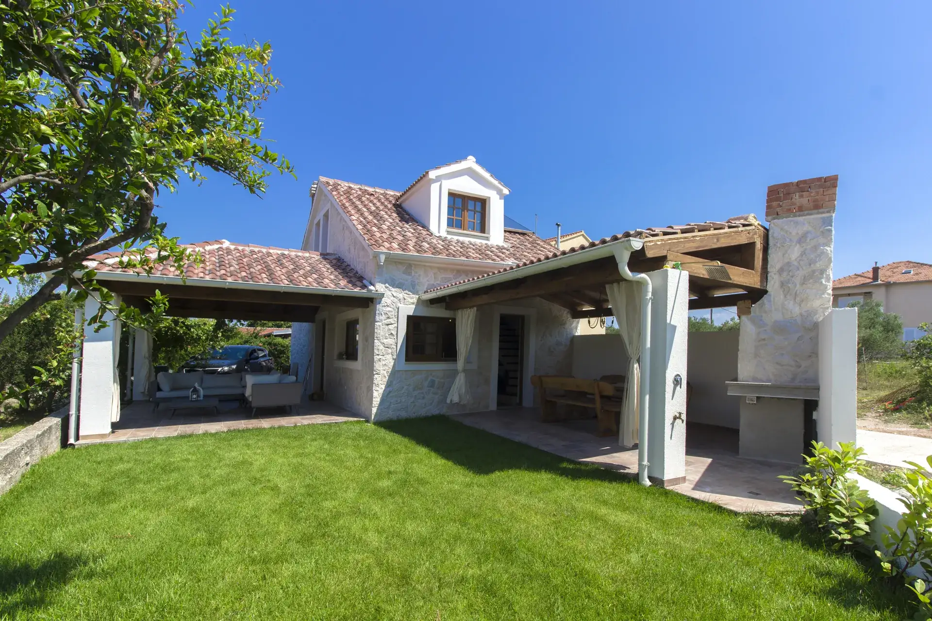 House Leila seen from the garden, with the lawn, covered terrace and stone BBQ chimney