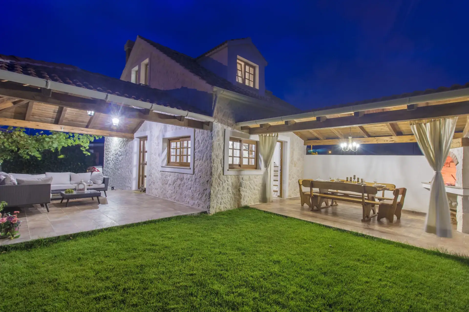 The lawn, covered terrace and dining pergola at House Leila lit up at dusk