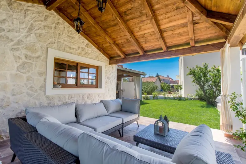 Outdoor lounge with cushioned sofas under the wooden pergola, looking onto the lawn